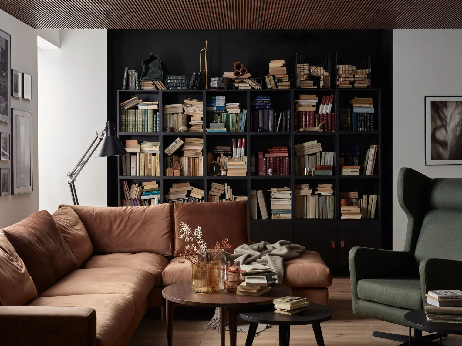 Przytulny salon z dużą biblioteczką pełną książek, brązową sofą narożną i zielonym fotelem typu uszak